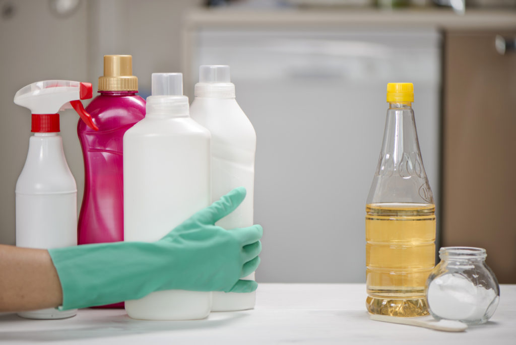 Hand moves chemical cleaners from table while letting vinegar remain.