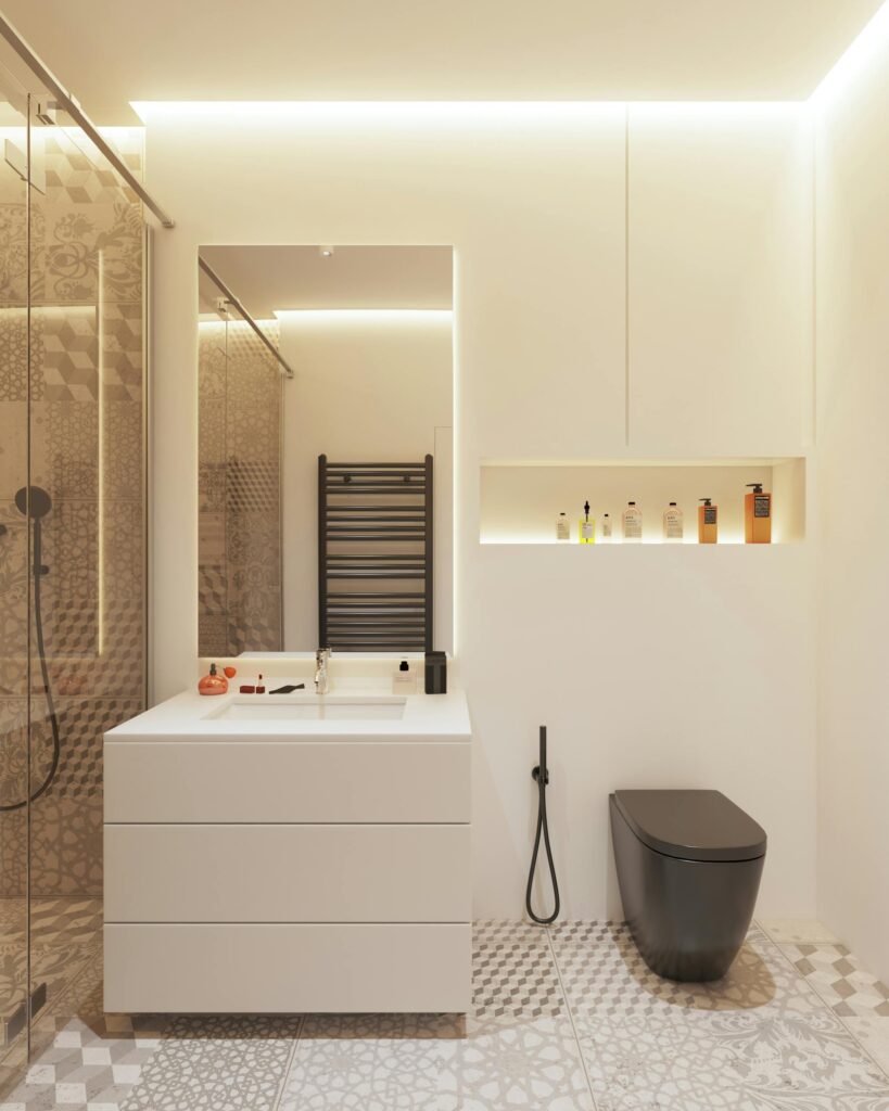 A modern ensuite bathroom with a geometric-patterned grey floor, white walls, a large illuminated mirror, and a black toilet