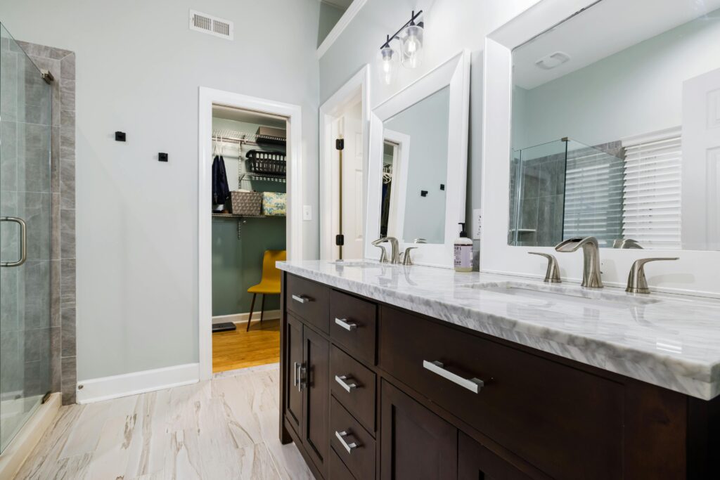 a Jack and Jill bathroom with grey marble worktops, a double sink, two mirrors, and a pale laminate floor