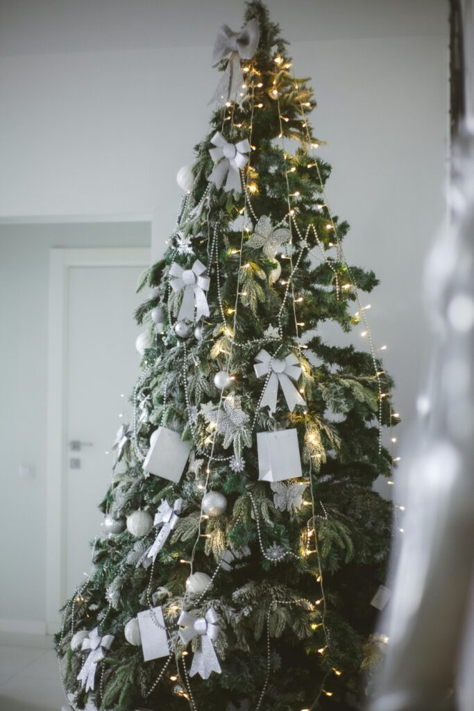 Christmas tree decorated in cool white baubles and bows, with warm fairy lights, inside a cool-toned home.
