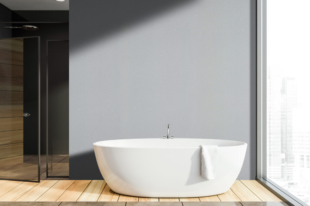 Interior of modern bathroom with dark gray walls, wooden floor, comfortable white bathtub standing near panoramic window and shower stall with glass doors.