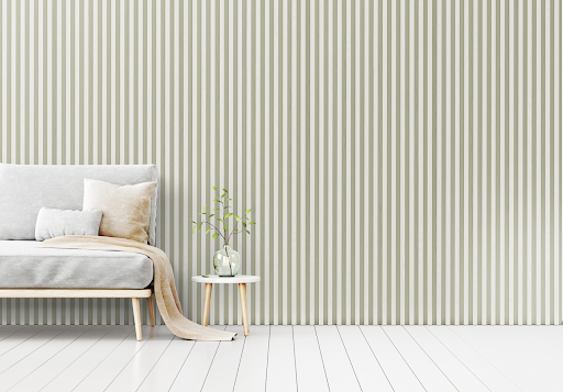 A room with a white slat panelled wall, white floorboards, and a light grey sofa next to a small coffee table.