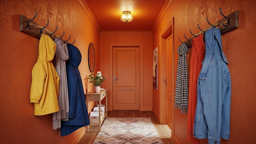 An orange colour-drenched hallway with coat hooks on either side, a patterned rug, a wooden cabinet, and a circular mirror on the wall.