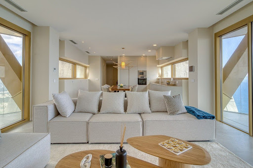 A cream and beige colour-drenched living room with a cream sofa, light wooden coffee tables, and large windows on either side of the room.