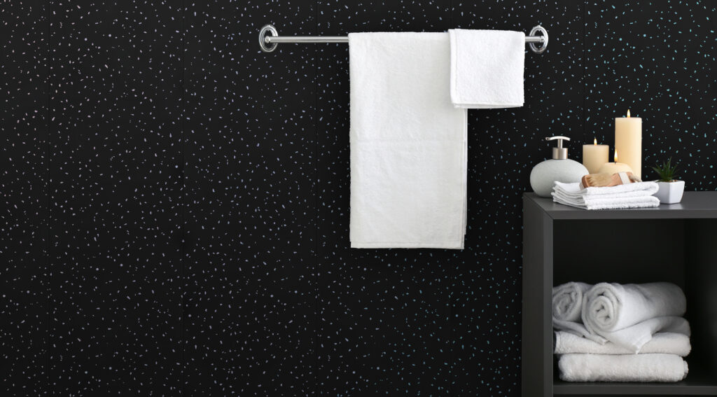 A black sparkle bathroom wall with white towels on a rail and a black cabinet in the corner.