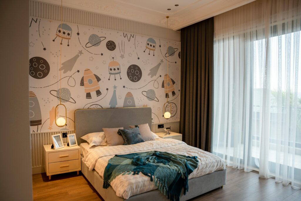 Children’s bedroom with cartoon and wall panel feature wall against a grey headboard. Two bedside tables next to a large bed with white and blue bedsheets.