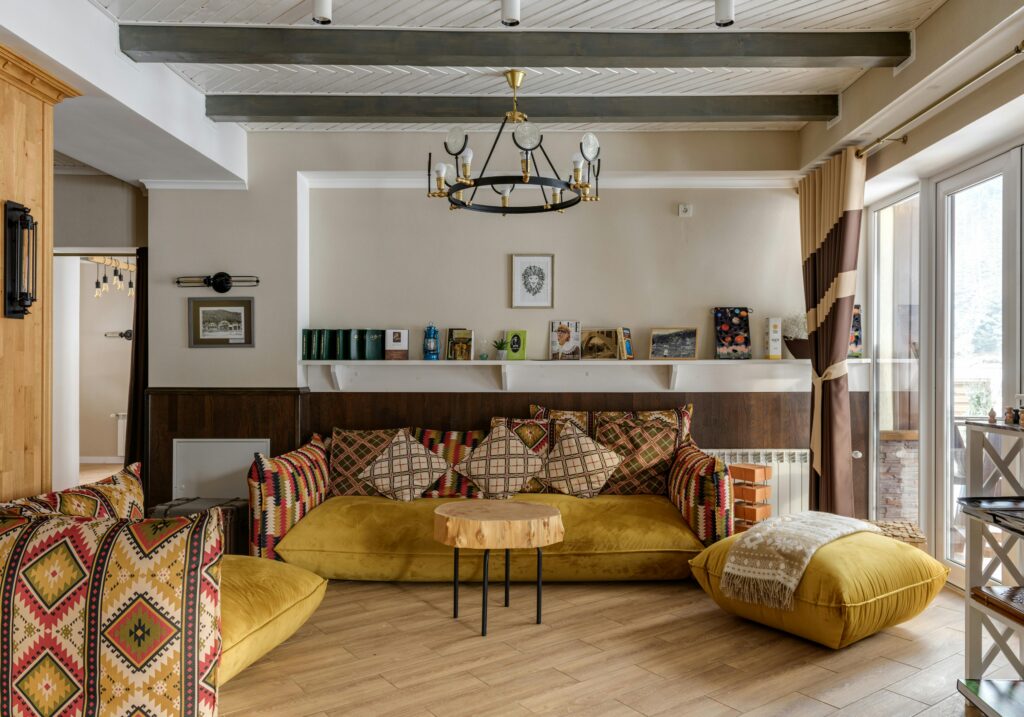 A sofa-scaped lounge with a yellow sofa and red patterned cushions, and a wooden coffee table in the centre of the room.