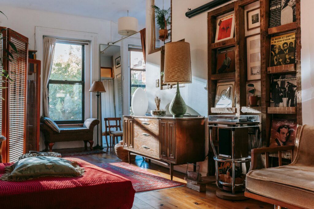 A maximalist room with a wooden cabinet and shelving, a red rug, framed prints and a tall lamp.