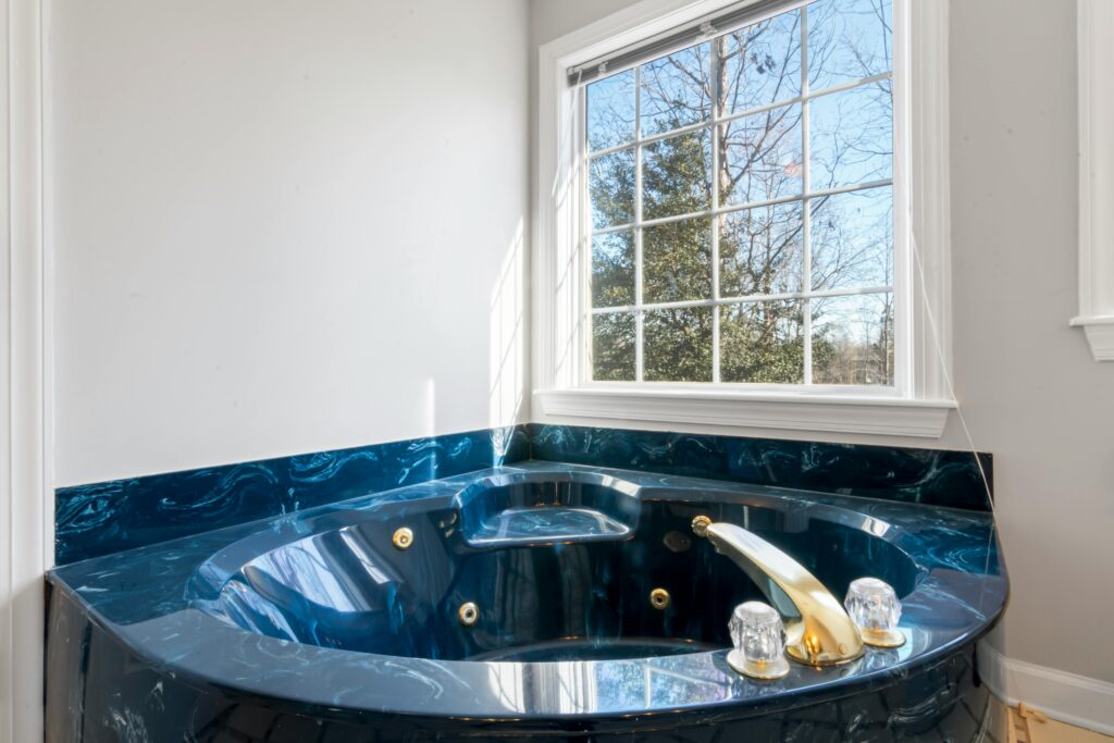 A blue marble whirlpool corner bath, fitted below a large, panelled window and featuring a gold tap.